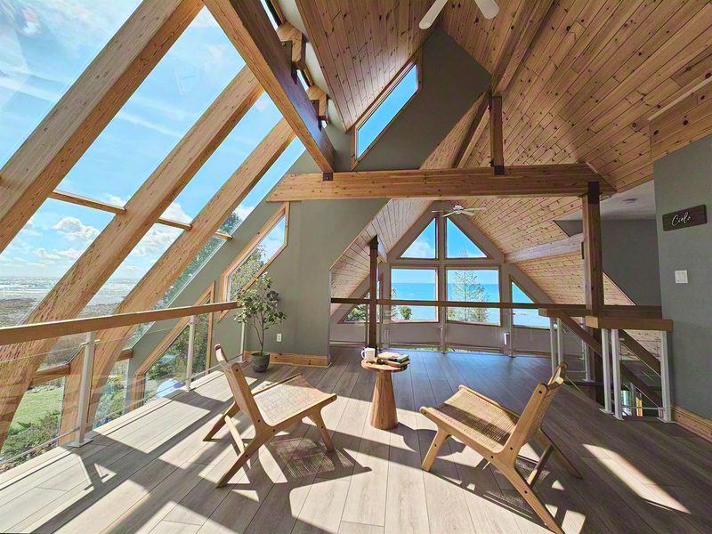 The Cielo loft at Casolena: angled sky glass following the roofline on one side, gable windows over Lake Huron on the other, two rattan chairs between them