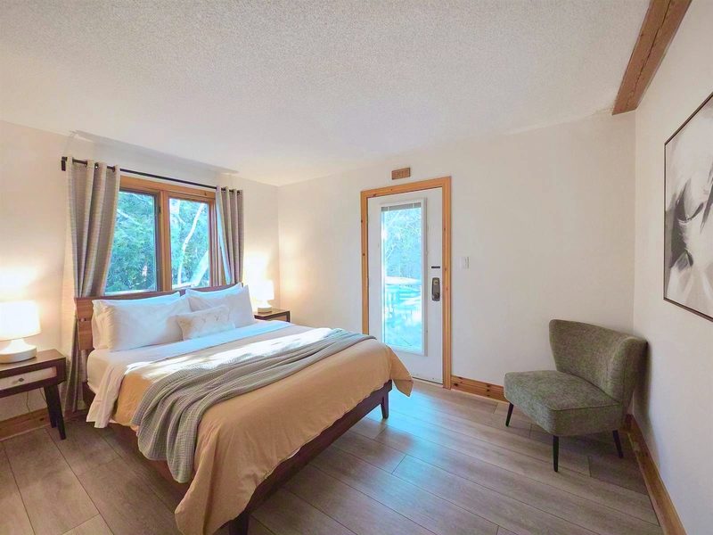 Alba bedroom with queen bed, a green armchair and morning light through the glass door