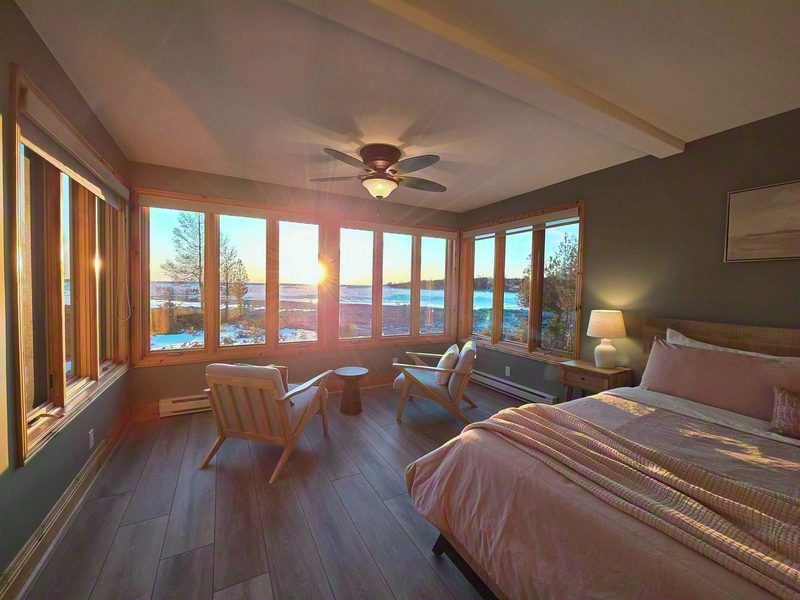 Delfina at sunset: the sun dropping straight ahead through windows on three sides, two chairs facing the lake and the king bed beside them