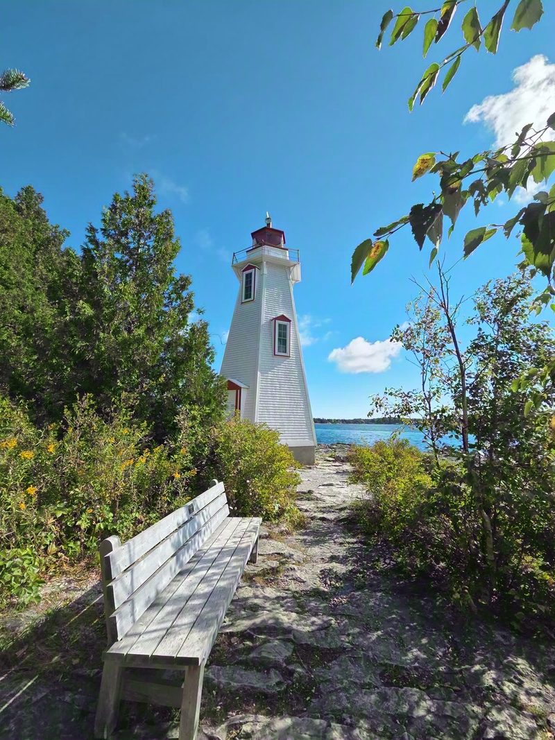 Big Tub Lighthouse and a white bench on the rocky point in summer