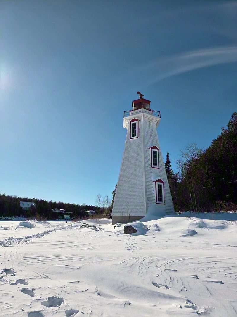 Big Tub Lighthouse, a white wooden tower with red trim, standing in deep untouched snow under a bright blue sky