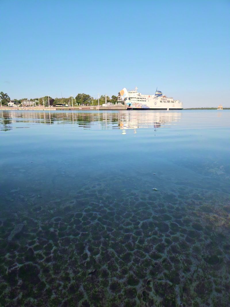 The Chi-Cheemaun at her berth across Little Tub Harbour in morning light, with cobble bottom visible through clear water