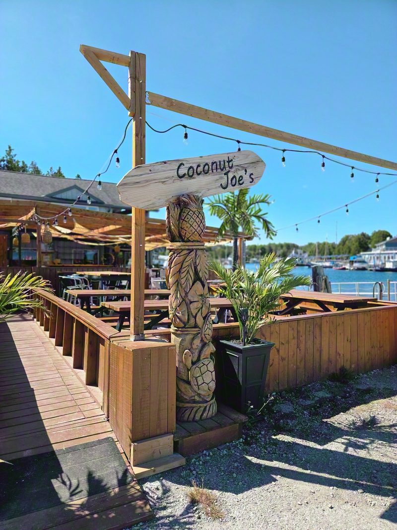 The carved Coconut Joe's sign on a wooden post beside the patio deck at Little Tub Harbour