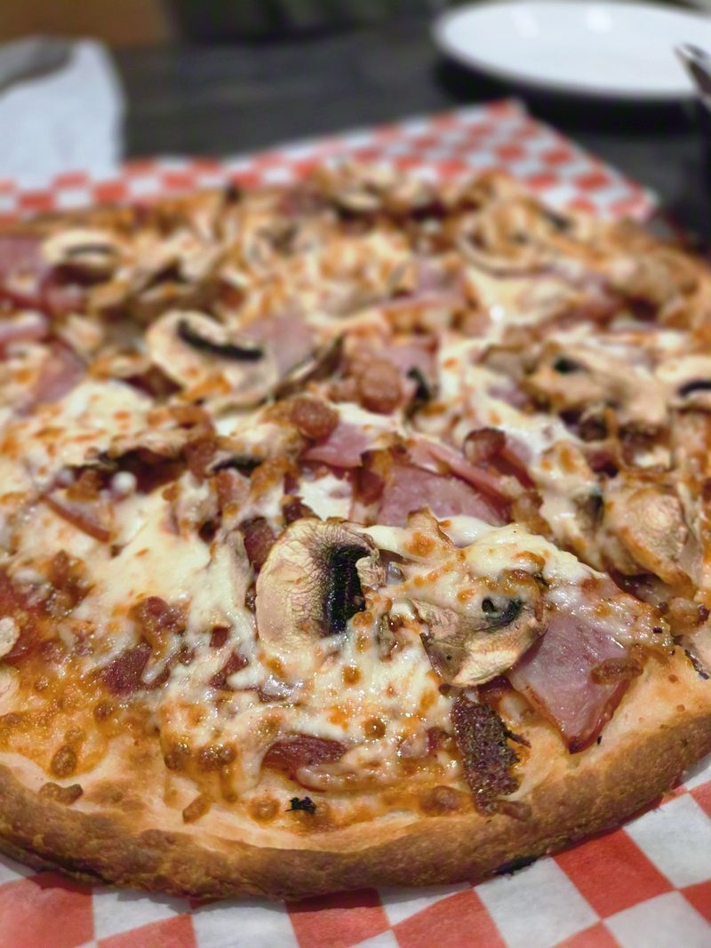 A pizza with ham, bacon and mushrooms on red checkered paper
