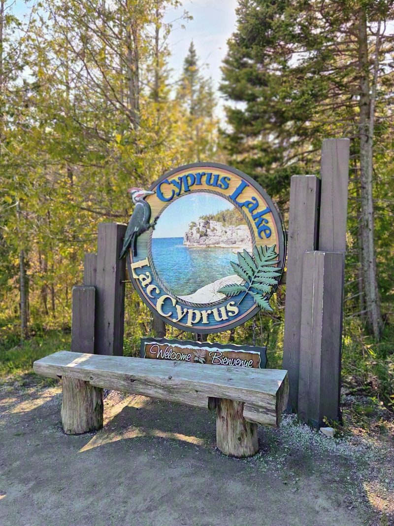 The carved Cyprus Lake and Lac Cyprus entrance sign beside a wooden bench at the park gate