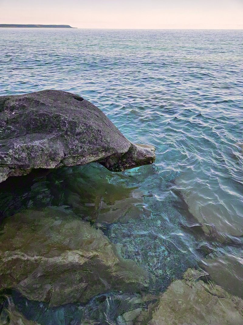 A large boulder standing in clear shallow water with rippled light on the bottom