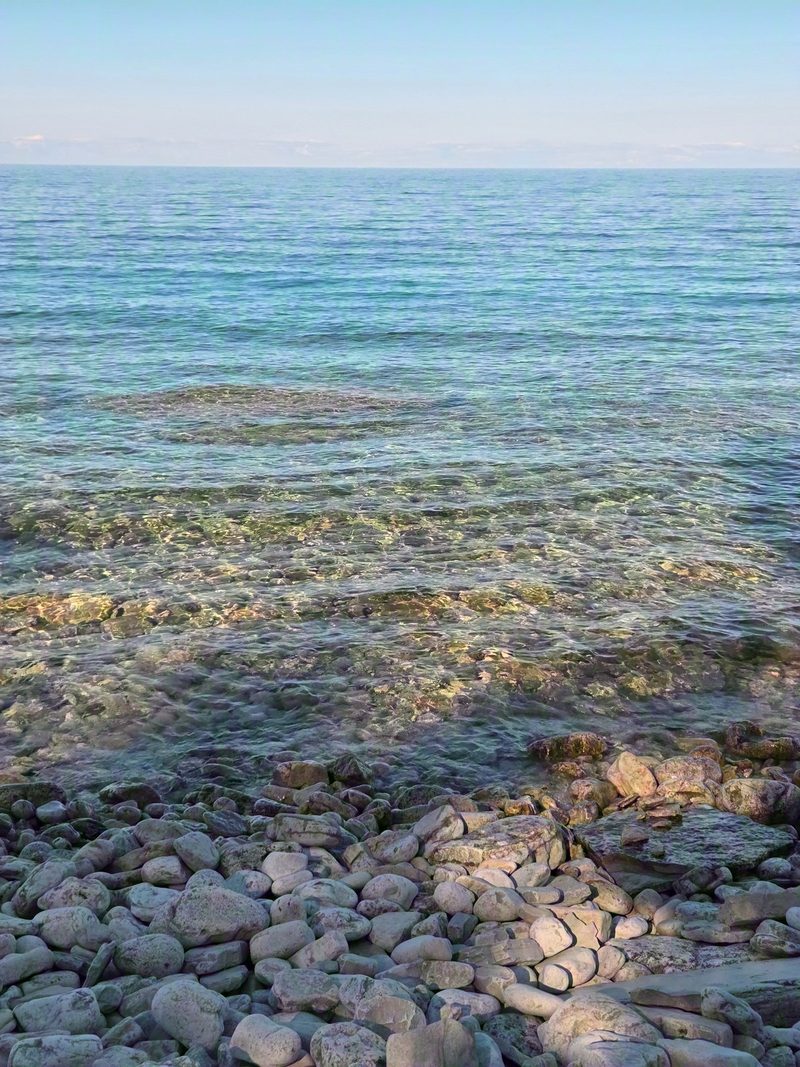 Clear shallow water over pale cobbles with the shade line crossing the bottom and a last patch of sun