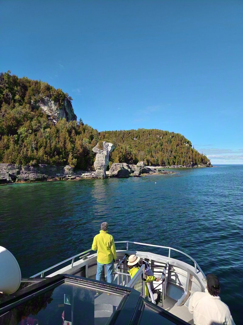 Passengers standing at the bow rail of the tour boat as the first flowerpot comes into view on the wooded limestone shoreline over turquoise water