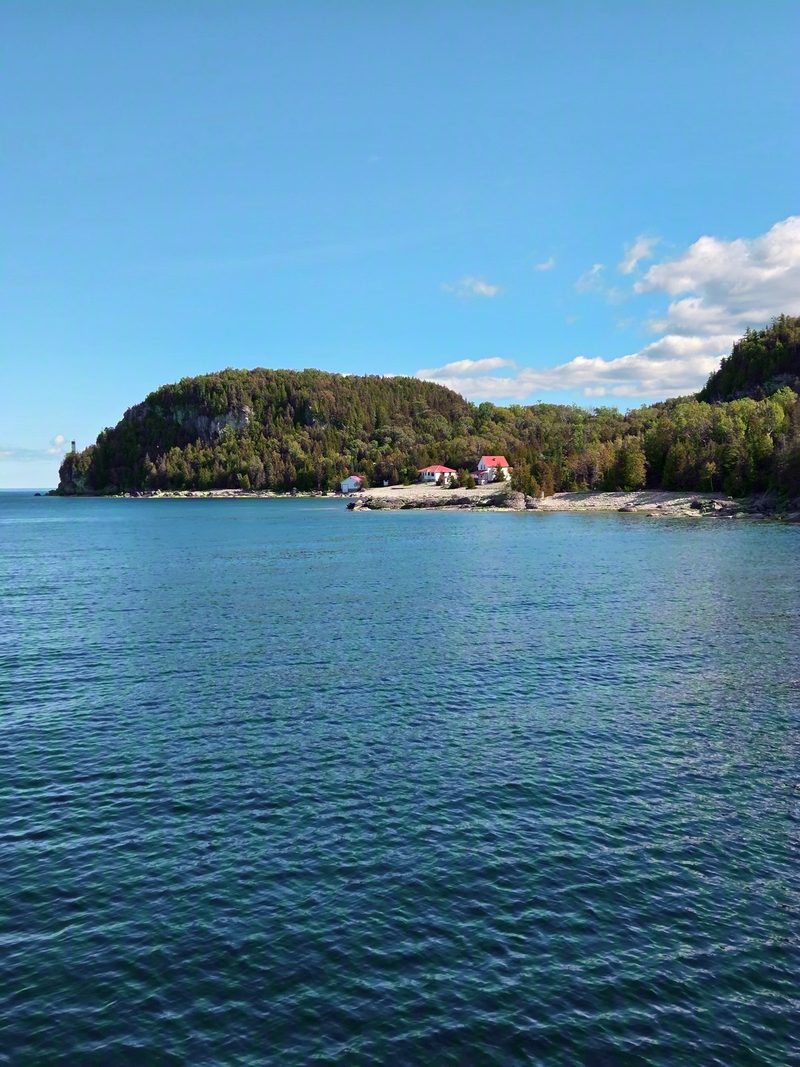 The red-roofed lightstation buildings on the wooded cliff of Flowerpot Island seen from the water