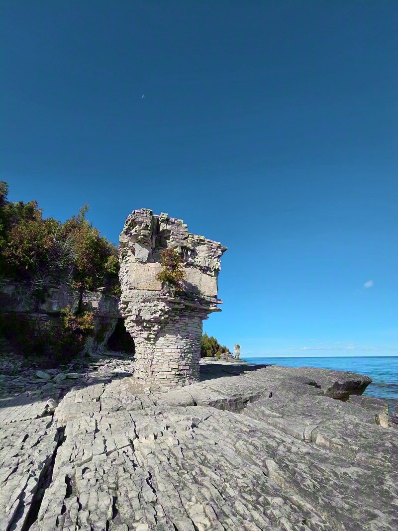 A flowerpot rock column seen along the limestone shore trail under a deep blue sky