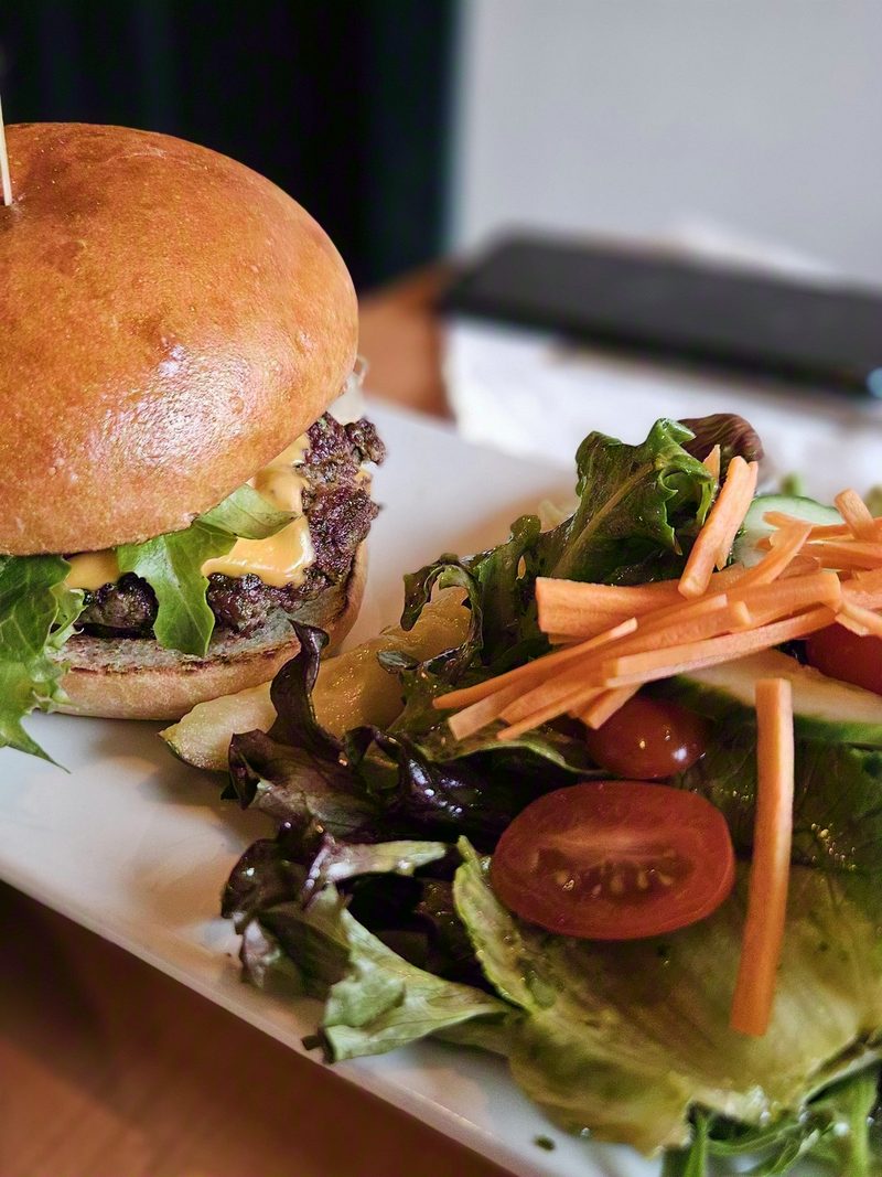A smash burger with cheddar and lettuce on a soft bun, plated beside a mixed green salad with carrot, cucumber and tomato