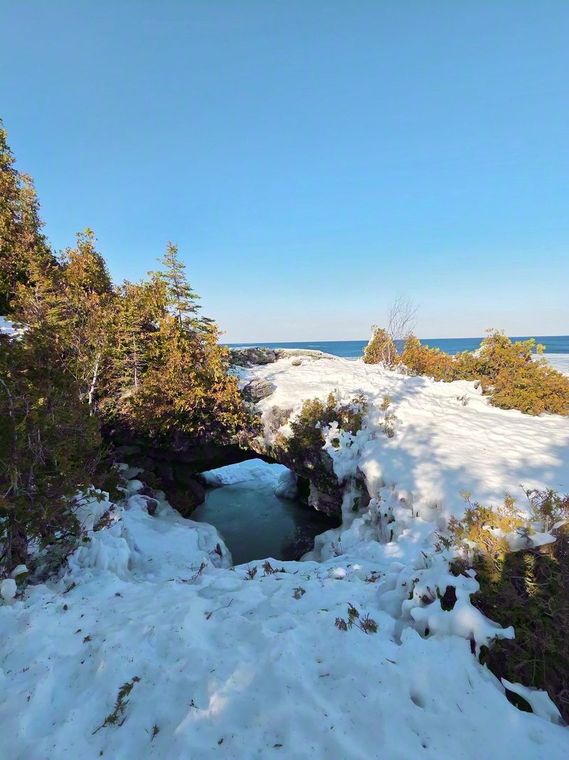 The Grotto's cave mouth under deep snow with pale turquoise ice filling the pool inside