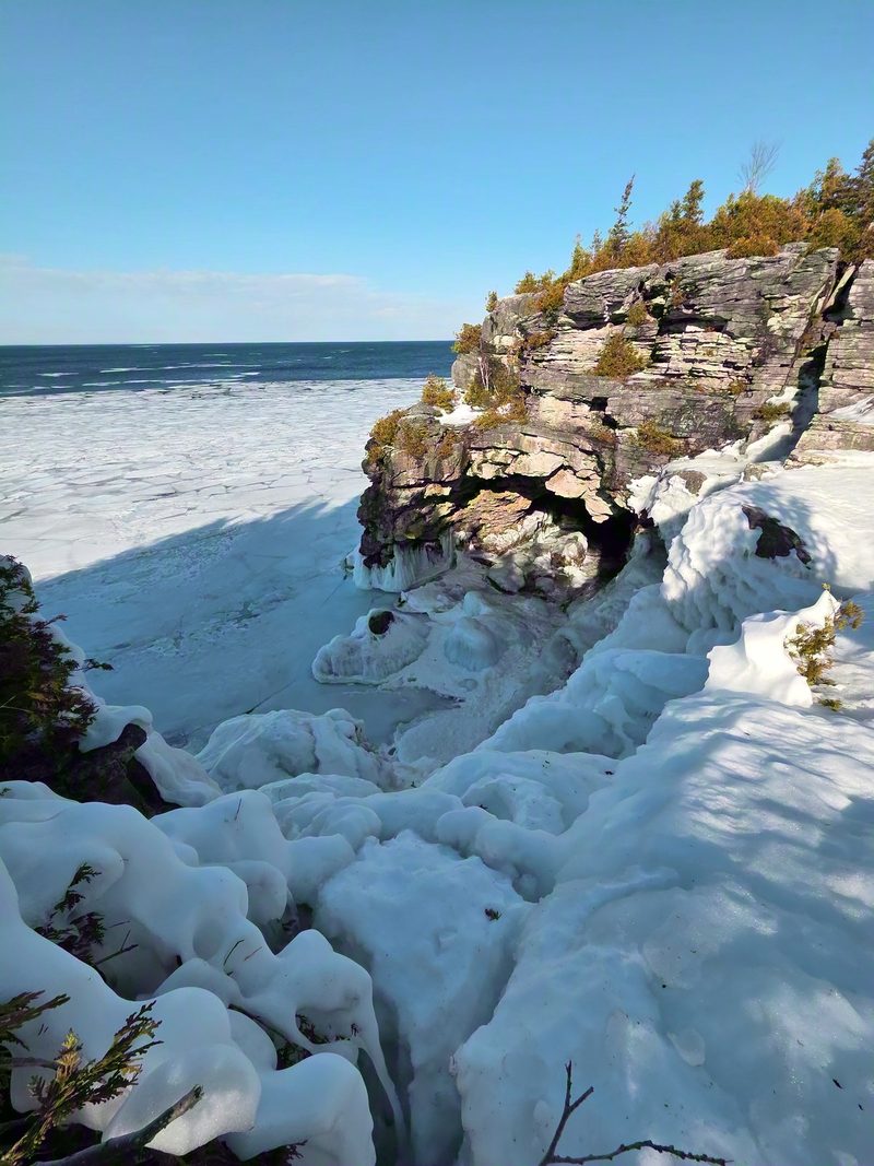 Limestone cliffs above the frozen bay with heavy snow drifts covering the cobble shoreline