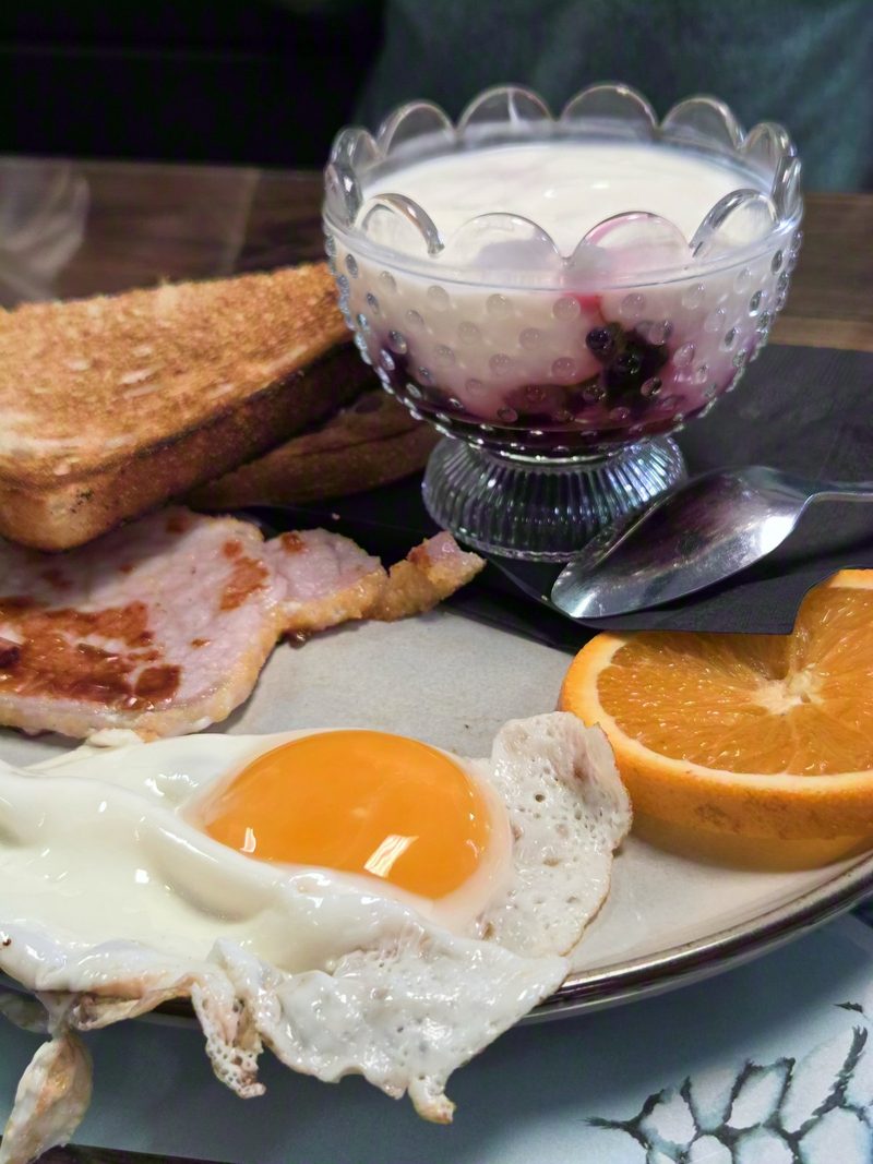 Fried egg, peameal bacon, toast and a berry parfait on a plate