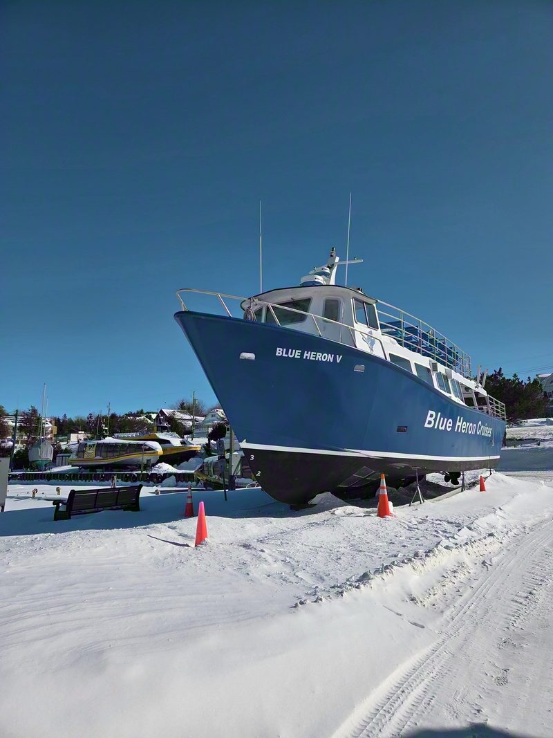 The bow of the Blue Heron V above a plowed snow-covered lot marked with orange cones