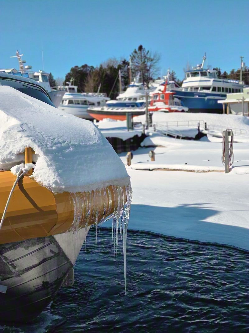 Icicles hanging from a snow-covered boat bow with dark open water of Little Tub Harbour directly below