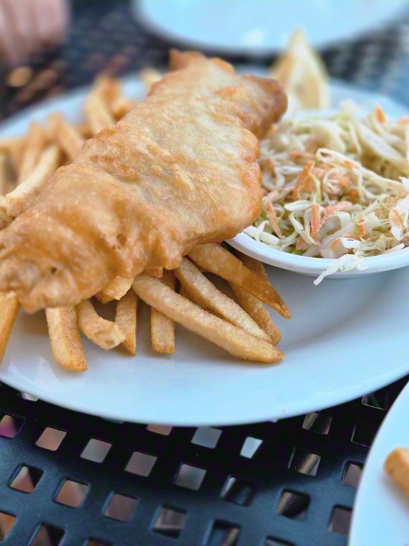 Battered whitefish and fries on a white plate at an outdoor table at Pharos