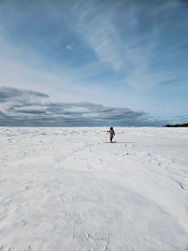 A lone snowshoer crossing a vast expanse of wind-sculpted snow under a bright blue sky