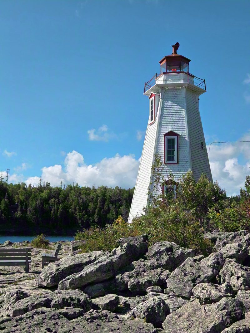 The white Big Tub Lighthouse above the rocky shore under a summer sky of cumulus clouds
