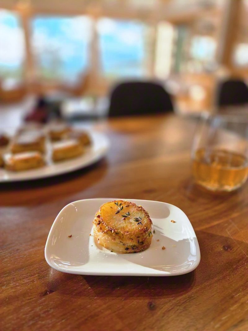 A small seared appetizer on a white plate at the dining table, the lake windows soft behind