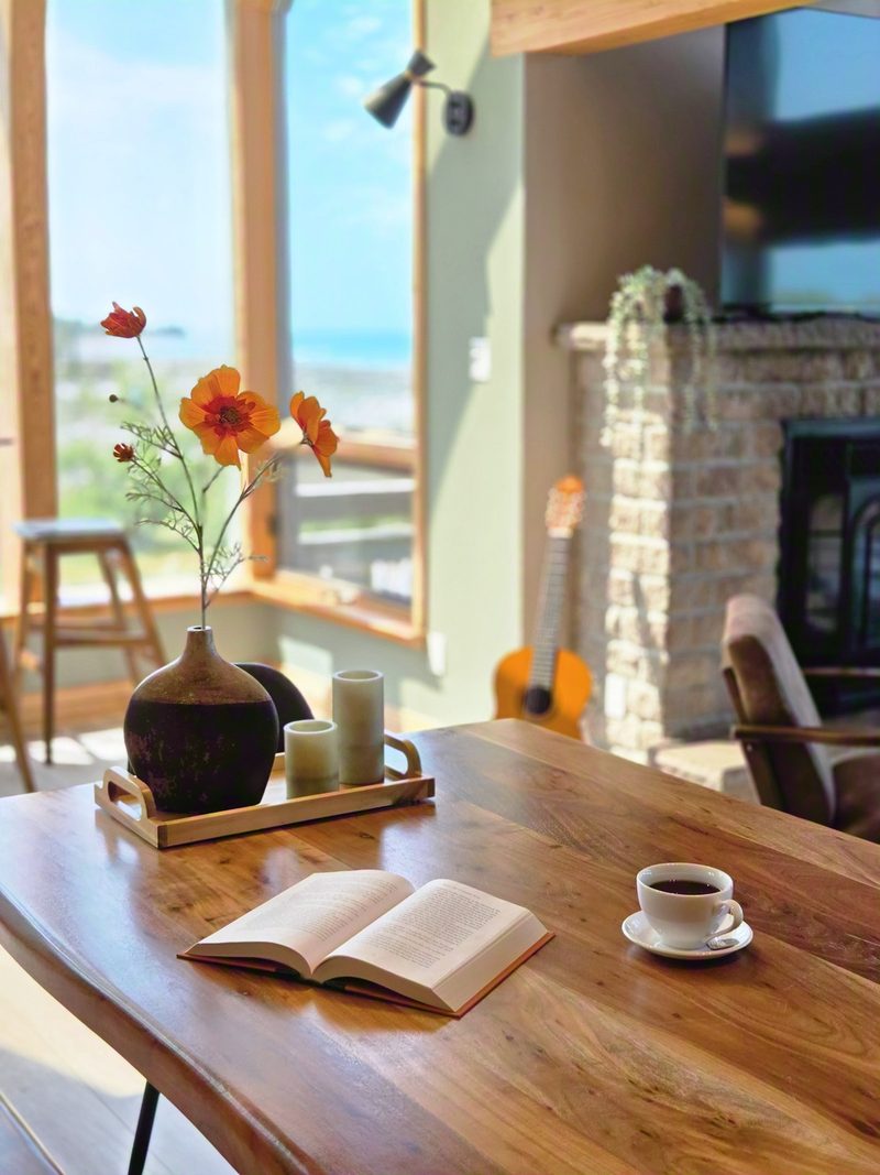 An open book and an espresso on the live-edge table with wildflowers in a vase and the guitar behind