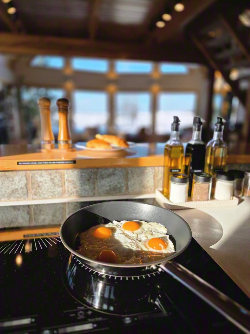 Eggs frying on the induction cooktop with oils, spices and the frozen lake beyond the window