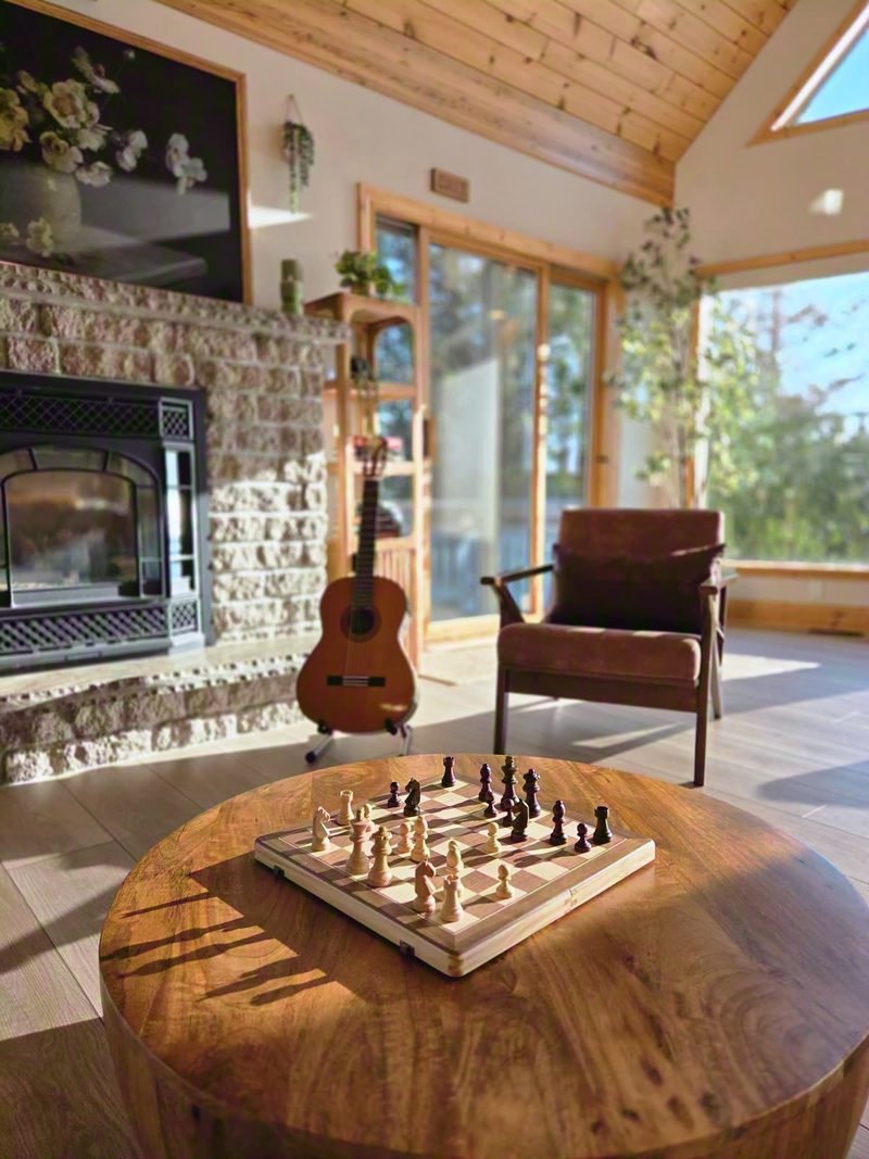 Chess set on a round wooden table in golden evening light, guitar and stone fireplace behind