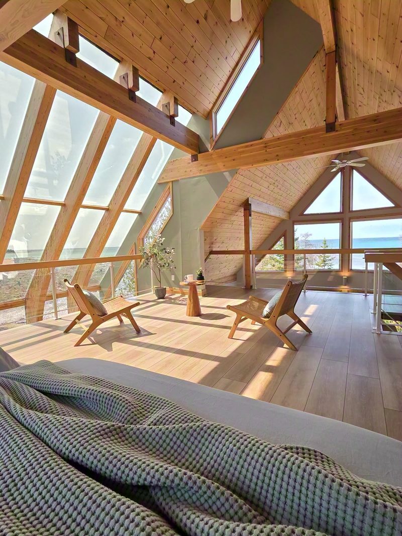 View from a bed in the Cielo loft across rattan chairs to the angled glass wall and lake