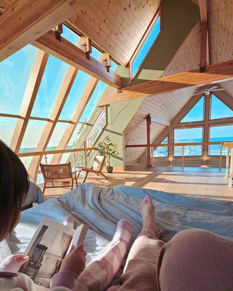 Reading in bed in the Cielo loft, feet up, with the angled glass wall and the lake beyond