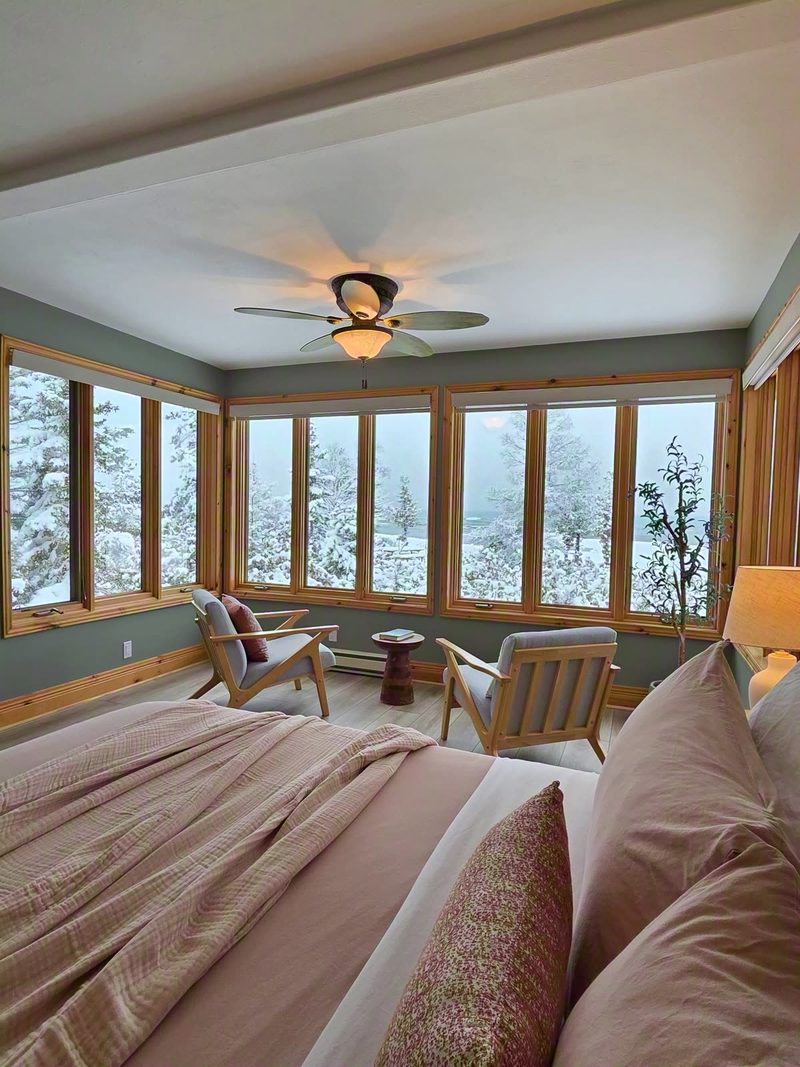 Delfina bedroom with soft pink bedding and wrap-around windows onto snowy cedars