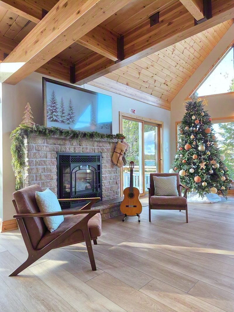 Stone fireplace hung with garland, a lit Christmas tree beside it and a guitar against the wall