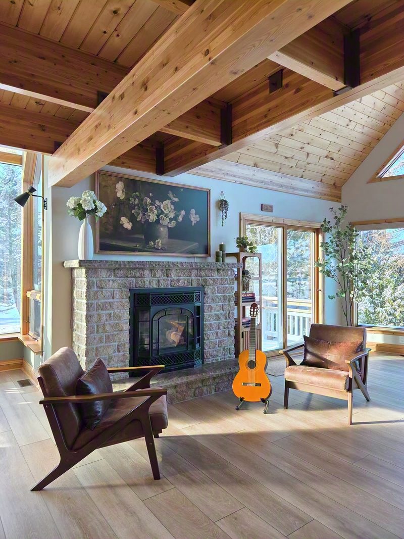 Stone fireplace with a propane stove, floral art above, two armchairs and a guitar in bright daylight
