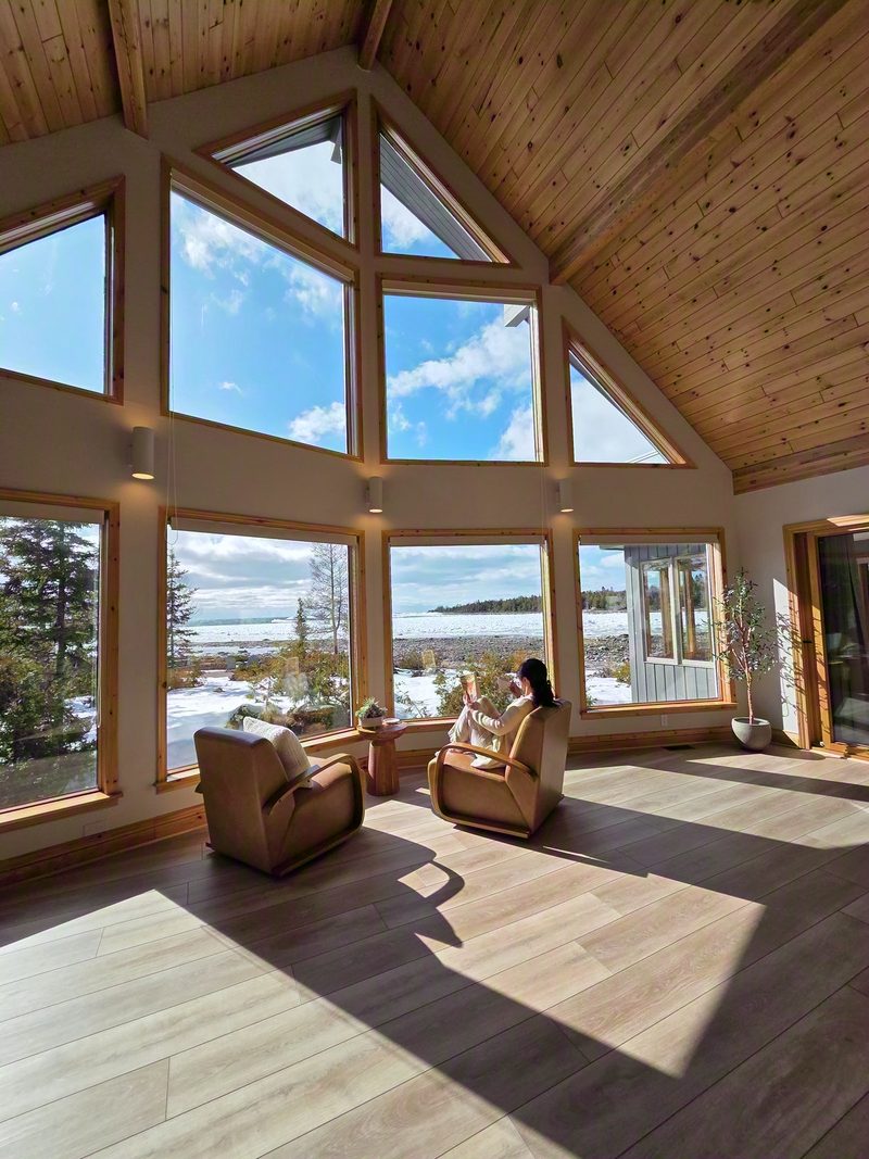 Two armchairs under the great room's cathedral windows with readers in them and snow on the shore outside