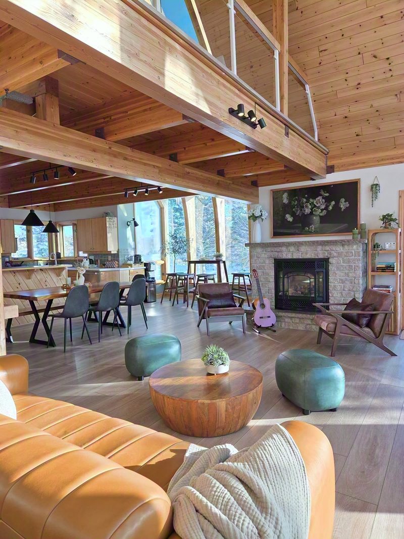 Open great room with leather sofa, fireplace, dining area, kitchen and the loft bridge above