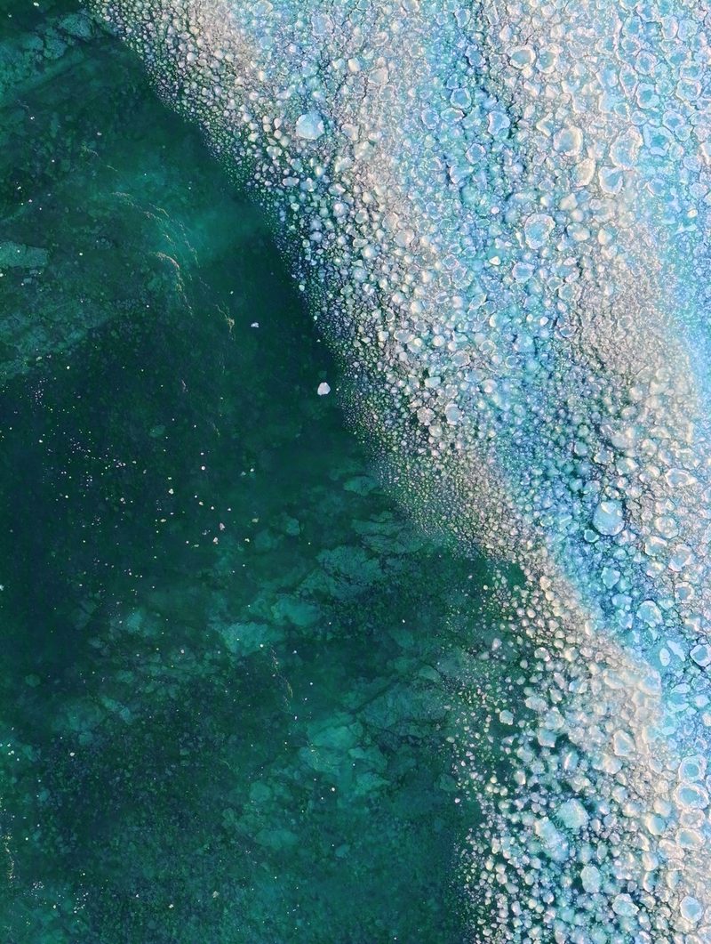 Frozen bubbles suspended in clear lake ice over deep green water at the shoreline