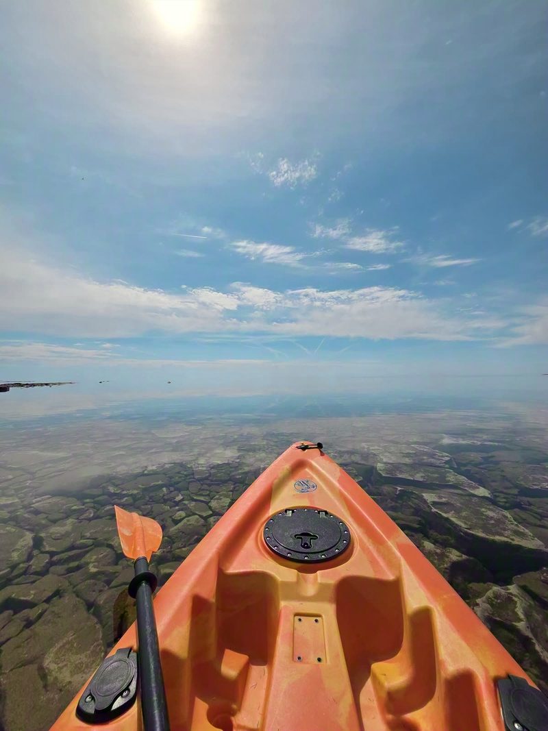 Bow of an orange kayak and a paddle on still open water under a big spring sky