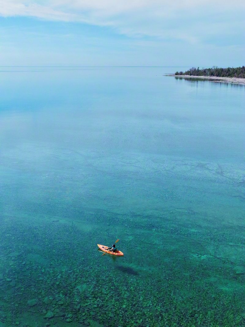 Aerial view of a lone kayak hanging over its own shadow on clear turquoise water