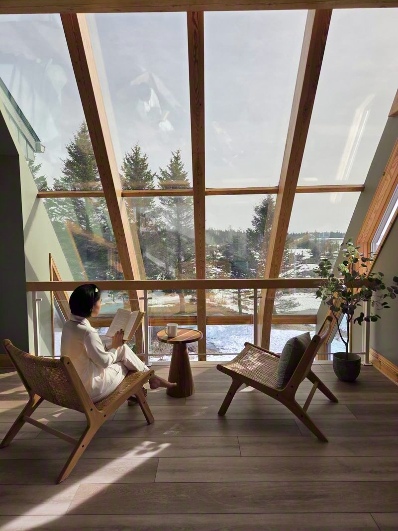 Reader in a woven chair by the loft's slanted glass wall with snowy trees outside