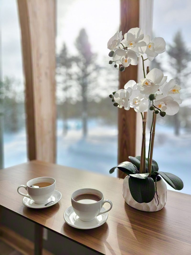 Two cups of tea and a white orchid on the window-side table with snowy trees outside