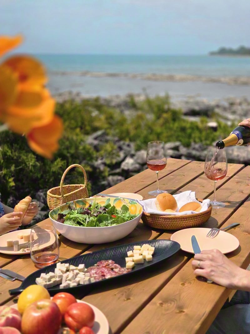 Lakeside picnic table set with charcuterie, salad, bread and wine being poured