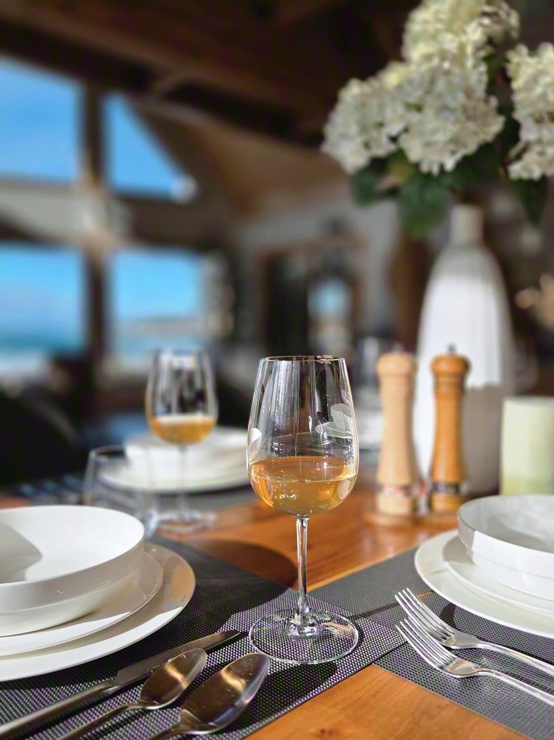 Close-up of white plates, cutlery and a glass of wine on the live-edge table in winter light