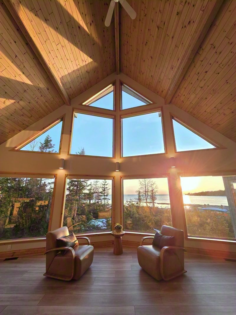Two armchairs in the sunroom facing the sun setting over the lake through wrap-around windows