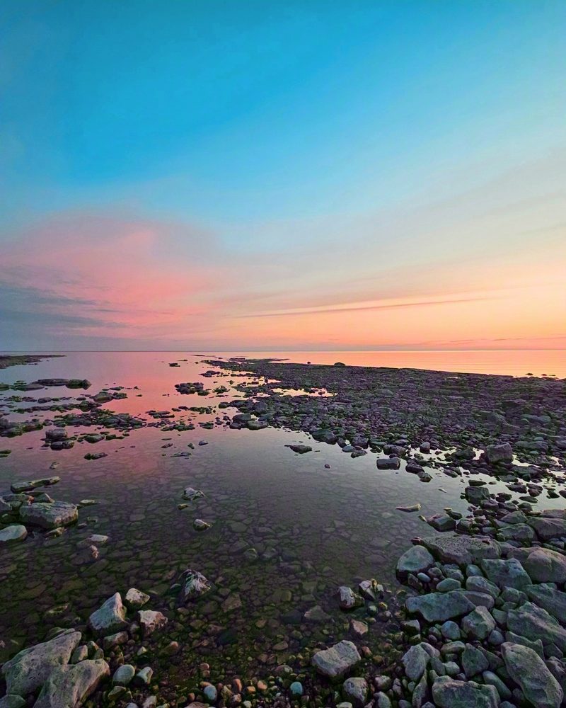 Pink and blue sunset over the flat limestone shelf and cobbles of the shoreline, the lake perfectly still