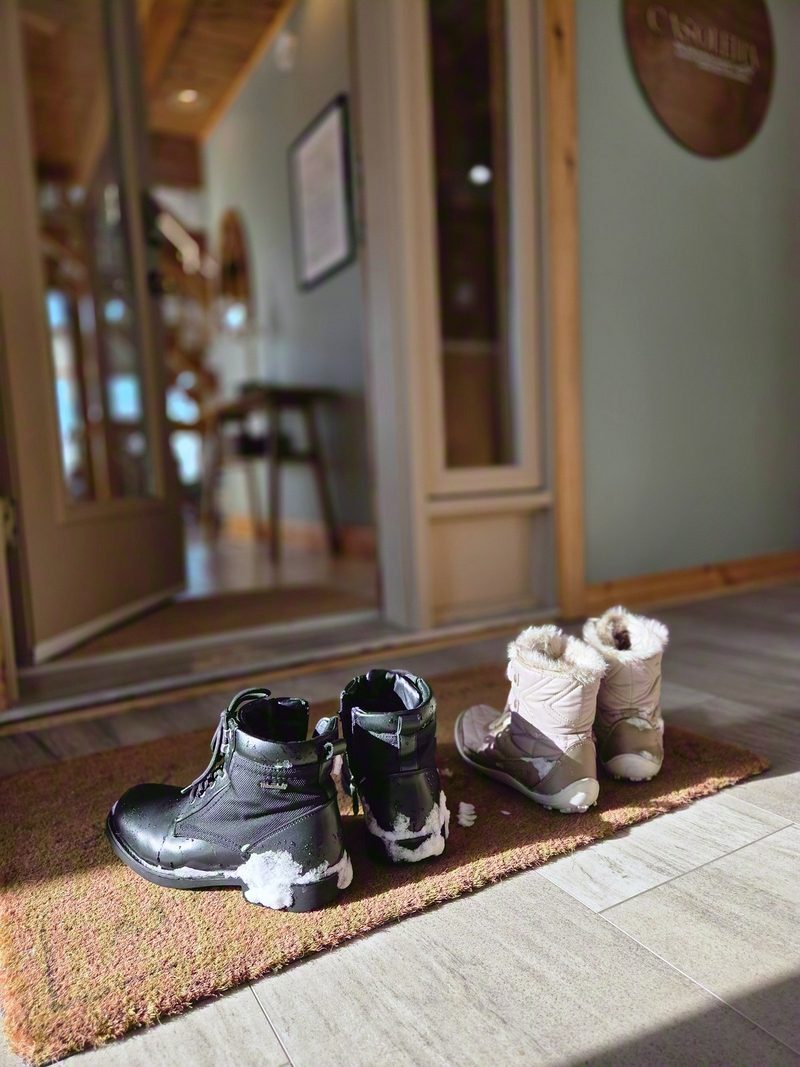 Snowy winter boots lined up on the mat inside the entry, the great room beyond the doorway