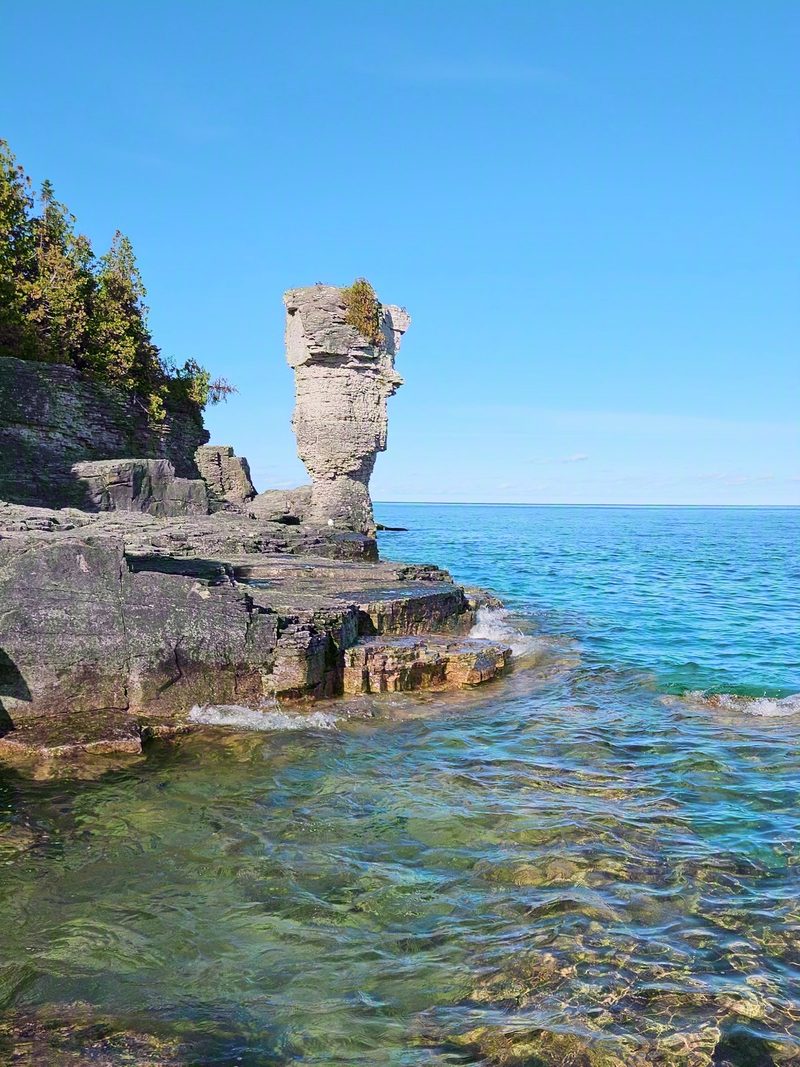 A flowerpot sea stack rising from the limestone shore above clear turquoise water