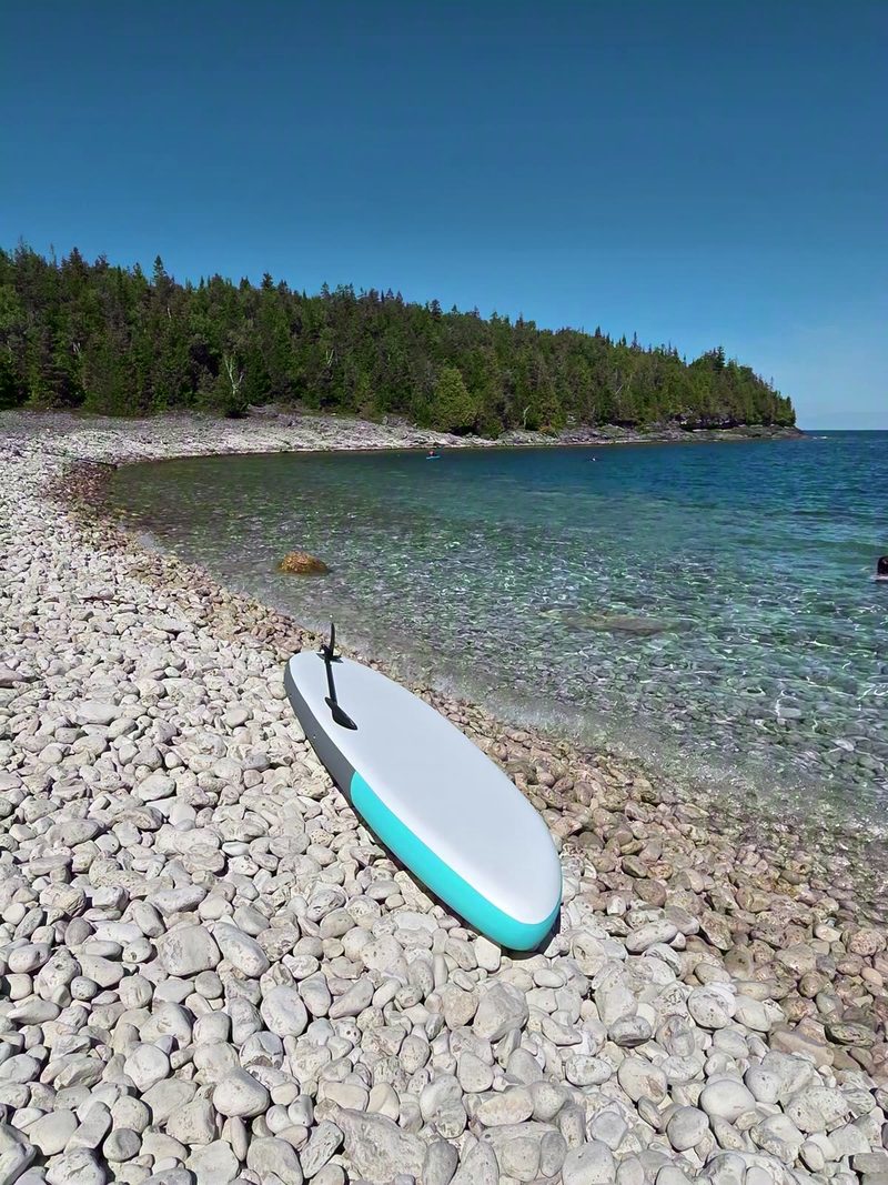A paddleboard resting on the white cobble beach at Little Cove beside clear turquoise water