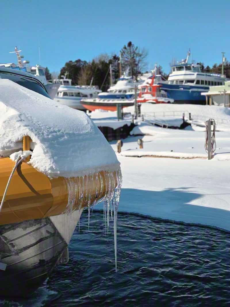 Tour boats under snow with icicles at their bows in frozen Little Tub Harbour